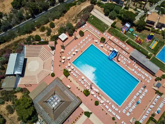 Vista dall'alto della piscina rettangolare con lettini, ombrelloni e area giochi gonfiabili per bambini