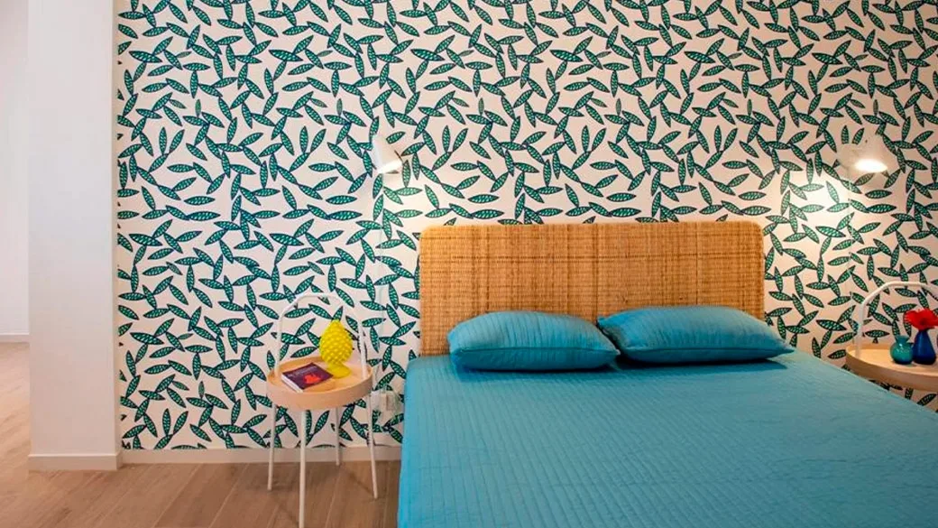 Camera con letto matrimoniale azzurro, testiera in rattan e parete decorata con foglie