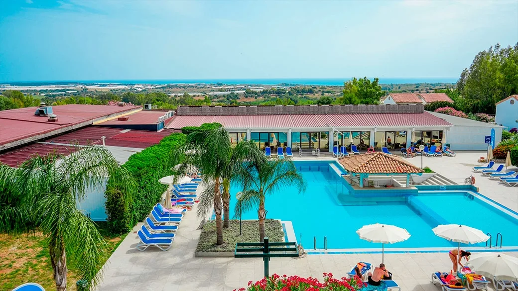 Piscina del resort con lettini blu, ombrelloni e vista panoramica sul mare