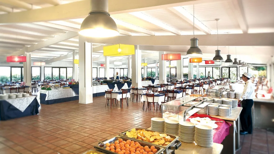Ampia sala ristorante a buffet con tavoli apparecchiati e piatti di frutta