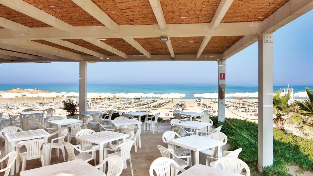 Terrazza ristorante coperta con tavoli bianchi e vista sulla spiaggia e sul mare