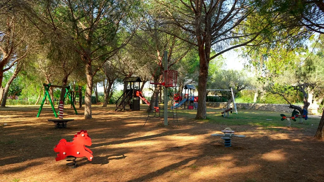 Area giochi per bambini all'ombra dei pini con altalene e scivoli