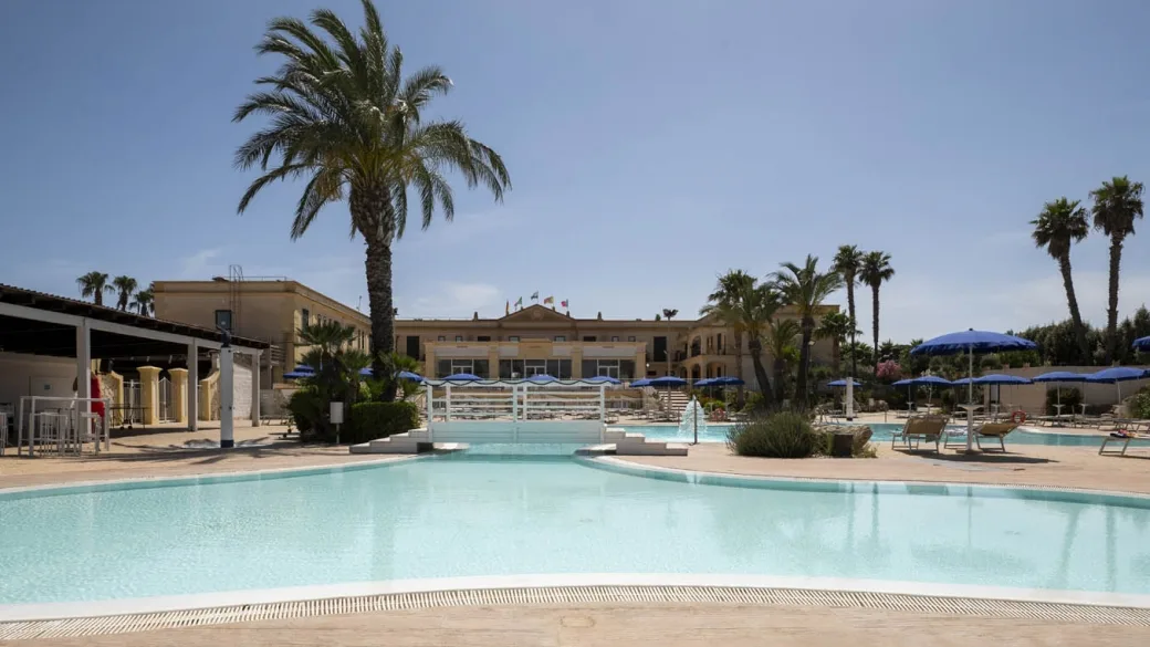 Ampia piscina con vista sull'edificio storico dell'hotel e ombrelloni blu