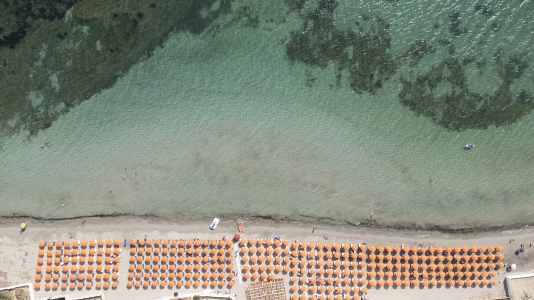 Vista aerea della spiaggia con file di ombrelloni arancioni e mare cristallino