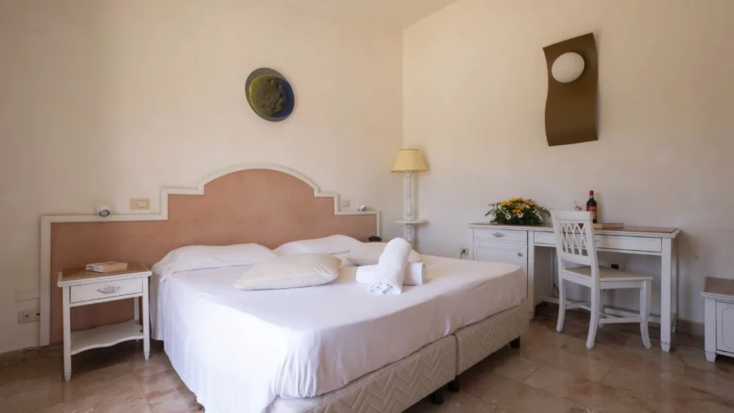 Camera matrimoniale con testiera rosa, scrivania bianca e pavimento in pietra