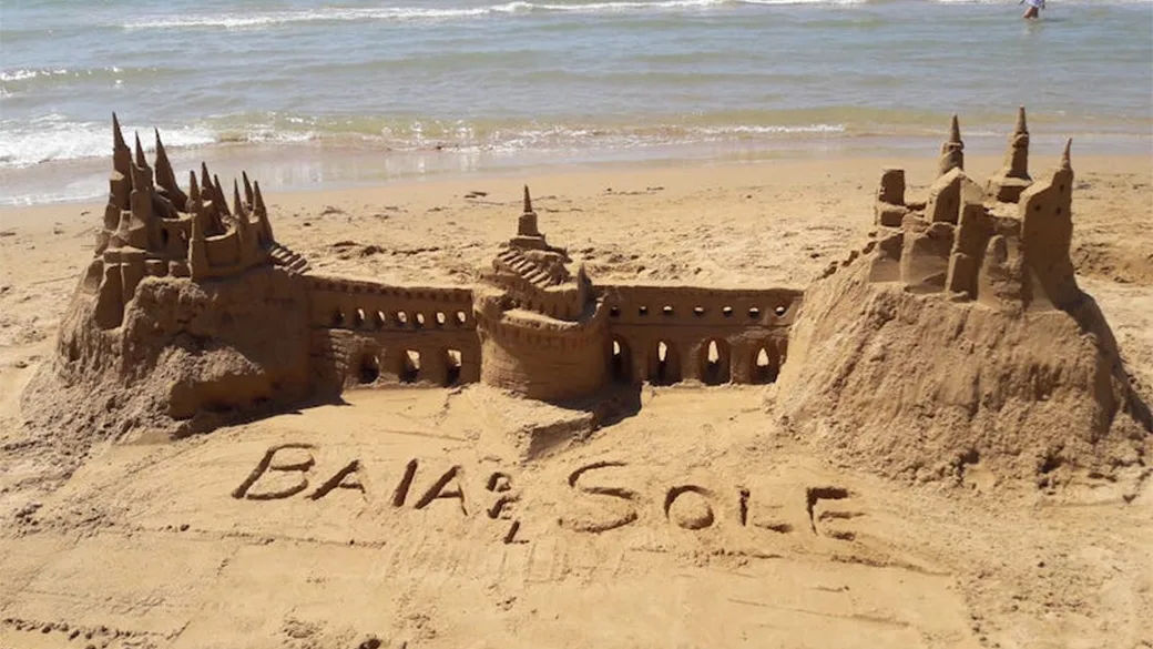 Castello di sabbia con scritta Baia del Sole sulla spiaggia
