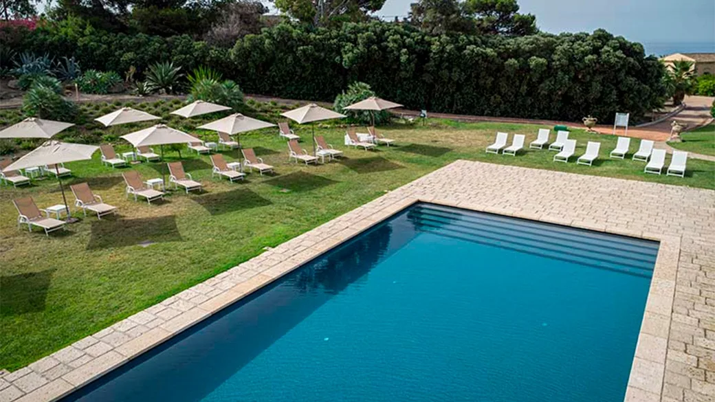 Piscina esterna con lettini, ombrelloni e giardino circostante