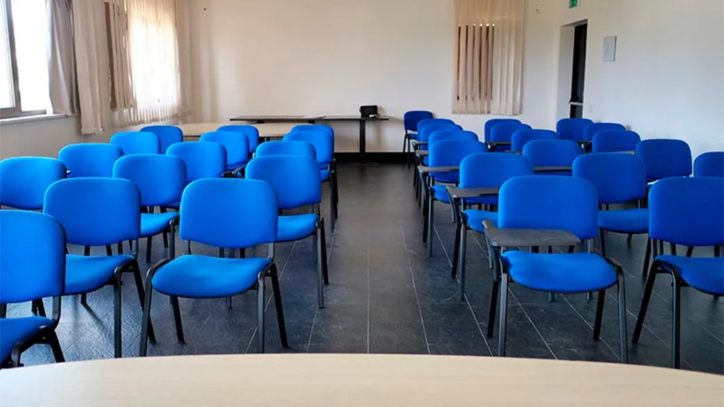 Sala riunioni con sedie blu disposte in file e tavolo relatore