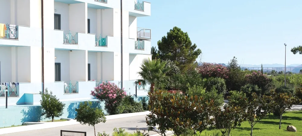 Esterno dell'edificio dell'hotel con balconi e giardino curato con palme e cespugli fioriti