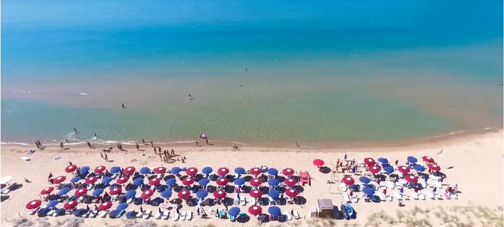 Spiaggia di sabbia con ombrelloni rossi e blu e mare cristallino visti dall'alto
