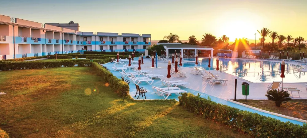 Piscina del resort al tramonto con lettini, ombrelloni chiusi, giardino e palme