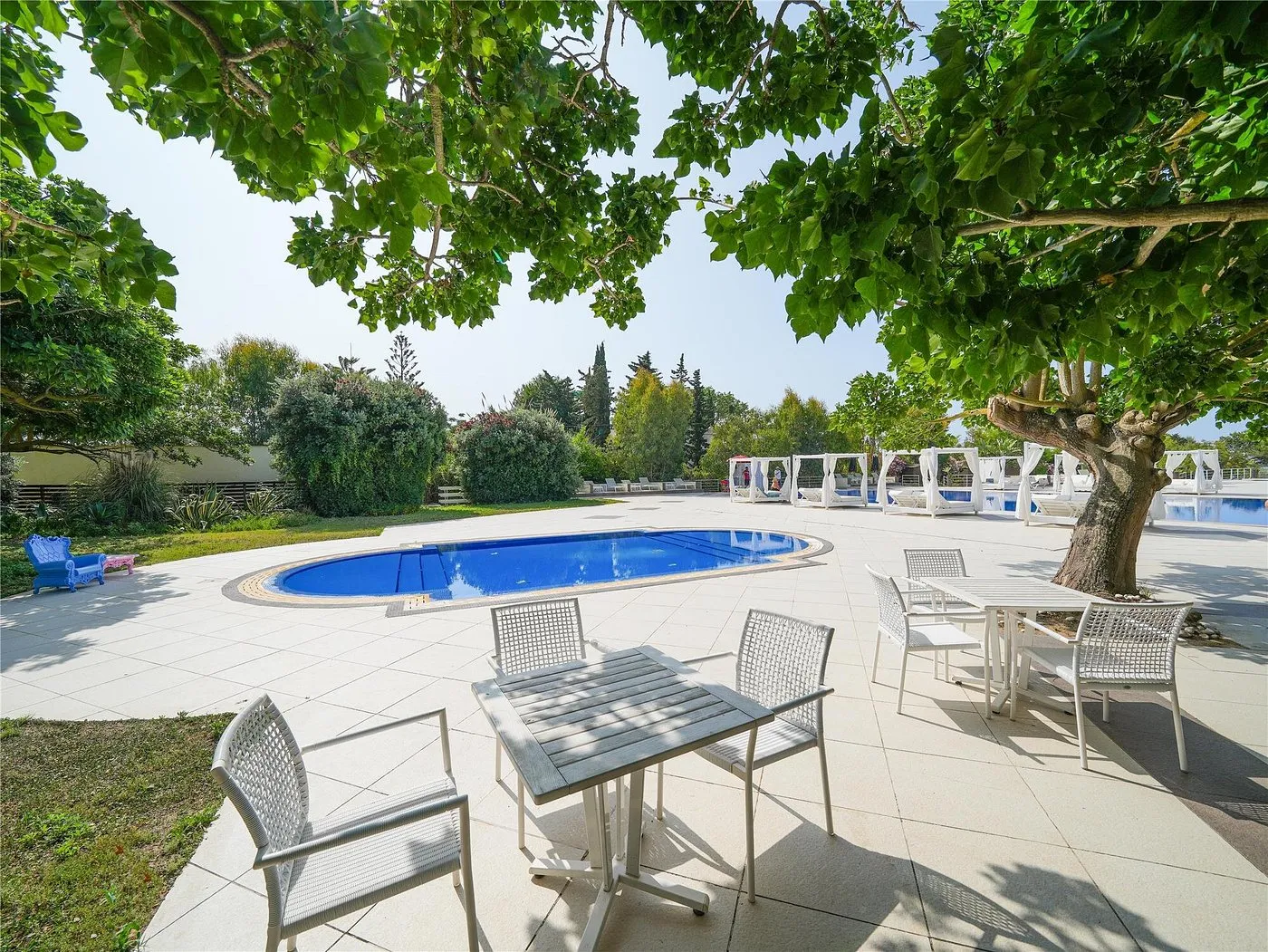 Piscina circolare con tavoli e sedie all'ombra degli alberi