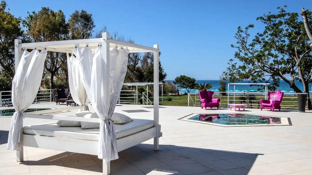 Terrazza con letto a baldacchino bianco, poltrone fucsia e vista sul mare