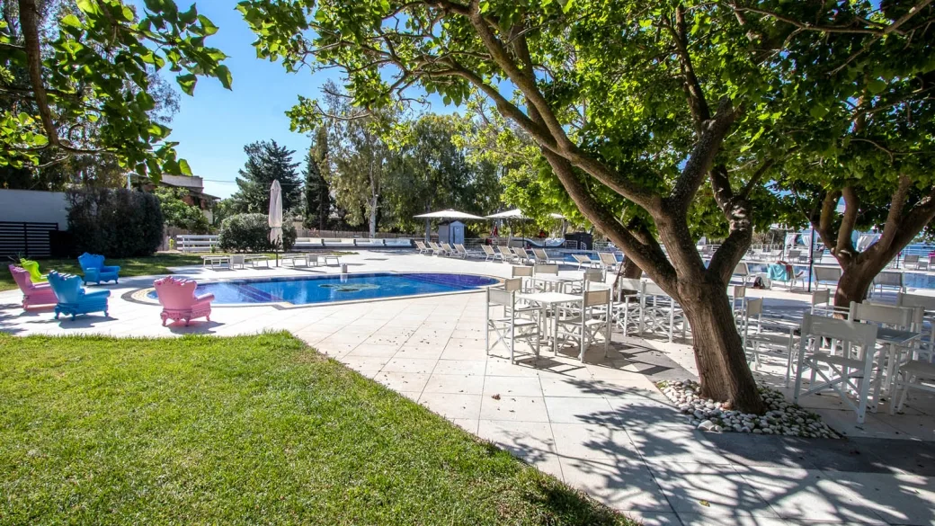 Giardino con piscina, poltrone colorate e tavoli all'ombra di un grande albero