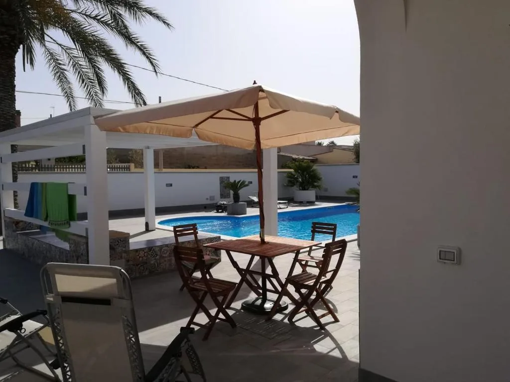 Terrazza con tavolo in legno, sedie e ombrellone affacciata sulla piscina