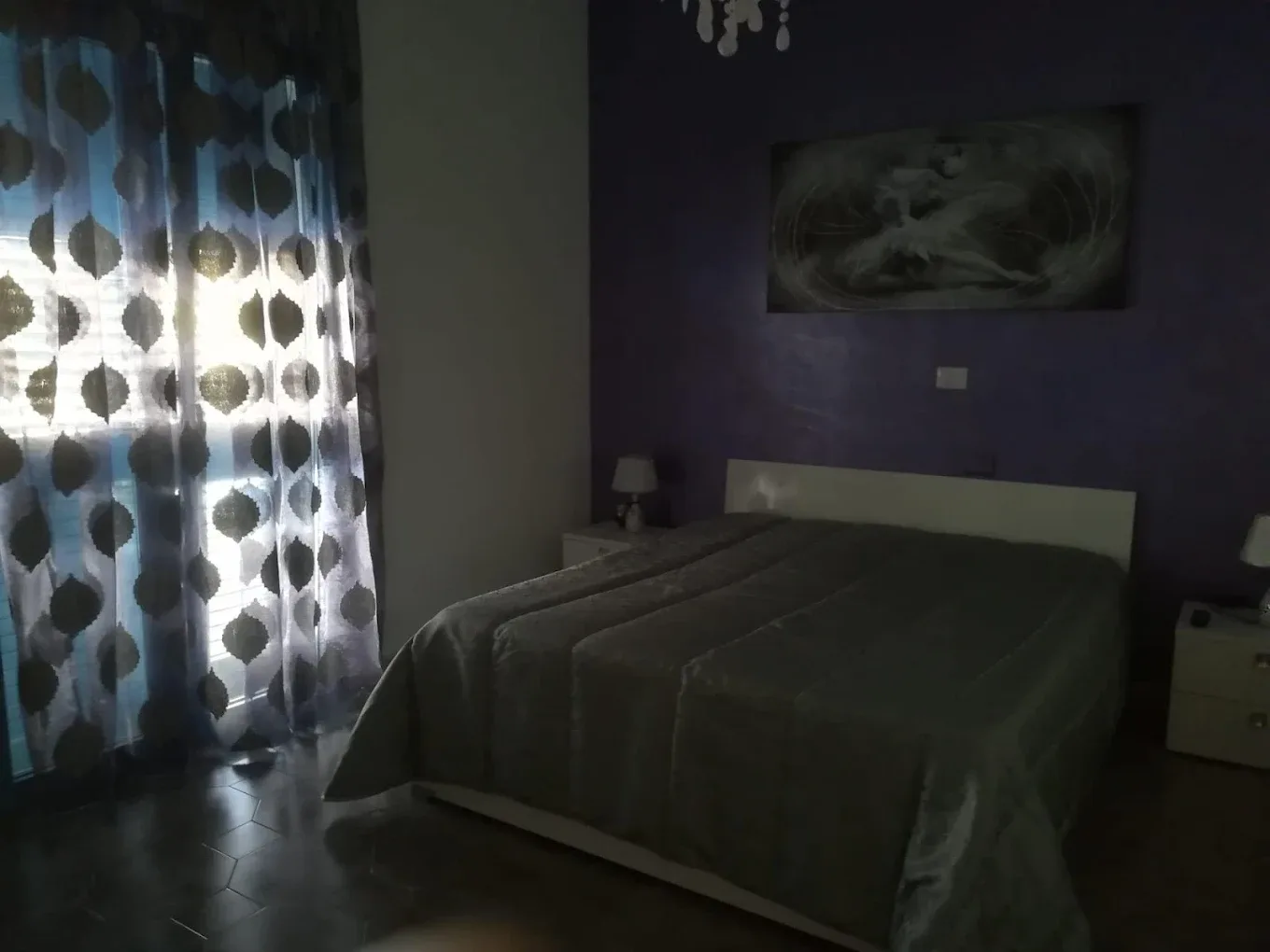 Camera da letto con pareti viola, letto matrimoniale, tende decorate e quadro sopra la testiera