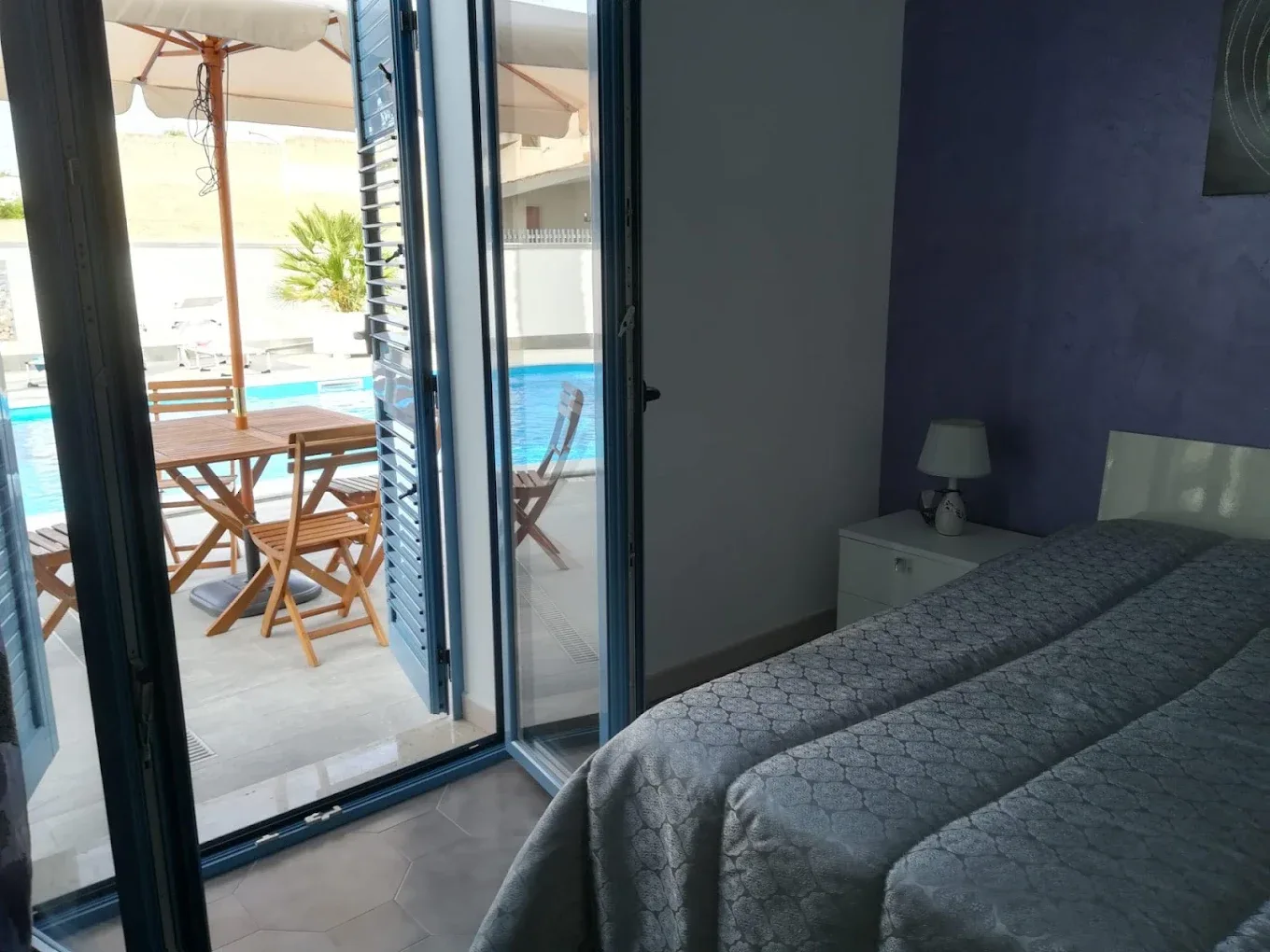 Camera da letto con parete viola e porta finestra affacciata sulla piscina e terrazza