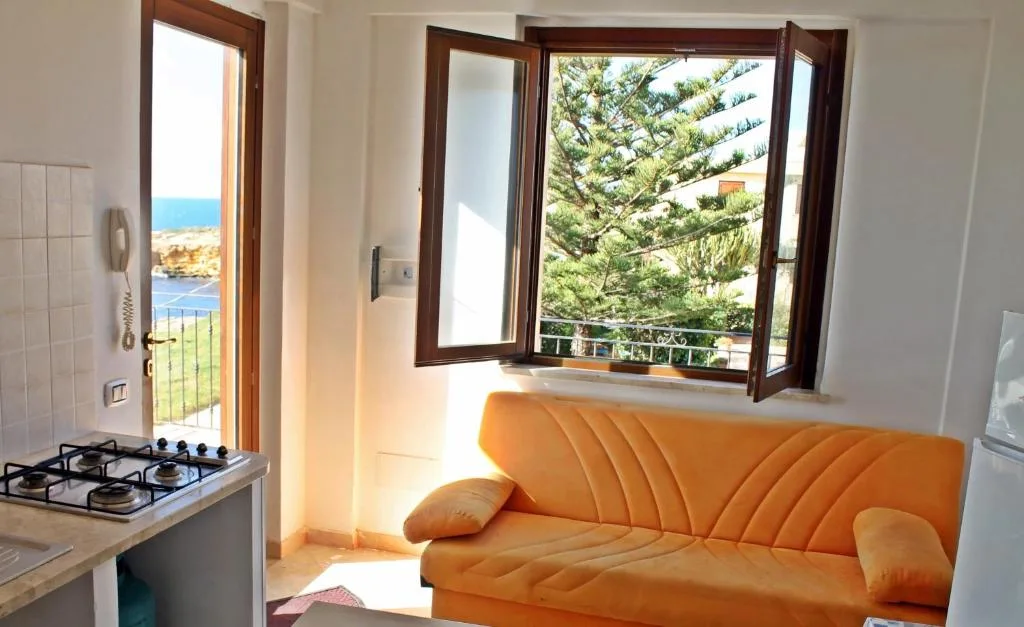 Soggiorno luminoso con divano arancione, angolo cottura e vista sul mare dalla finestra