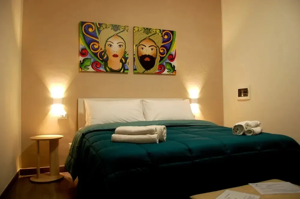 Camera con letto dal piumone verde e coloratissimi quadri di teste di moro