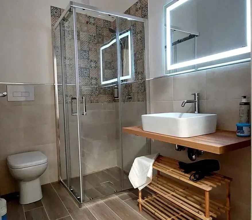 Bagno moderno con box doccia in vetro, lavabo su mensola in legno e specchio retroilluminato
