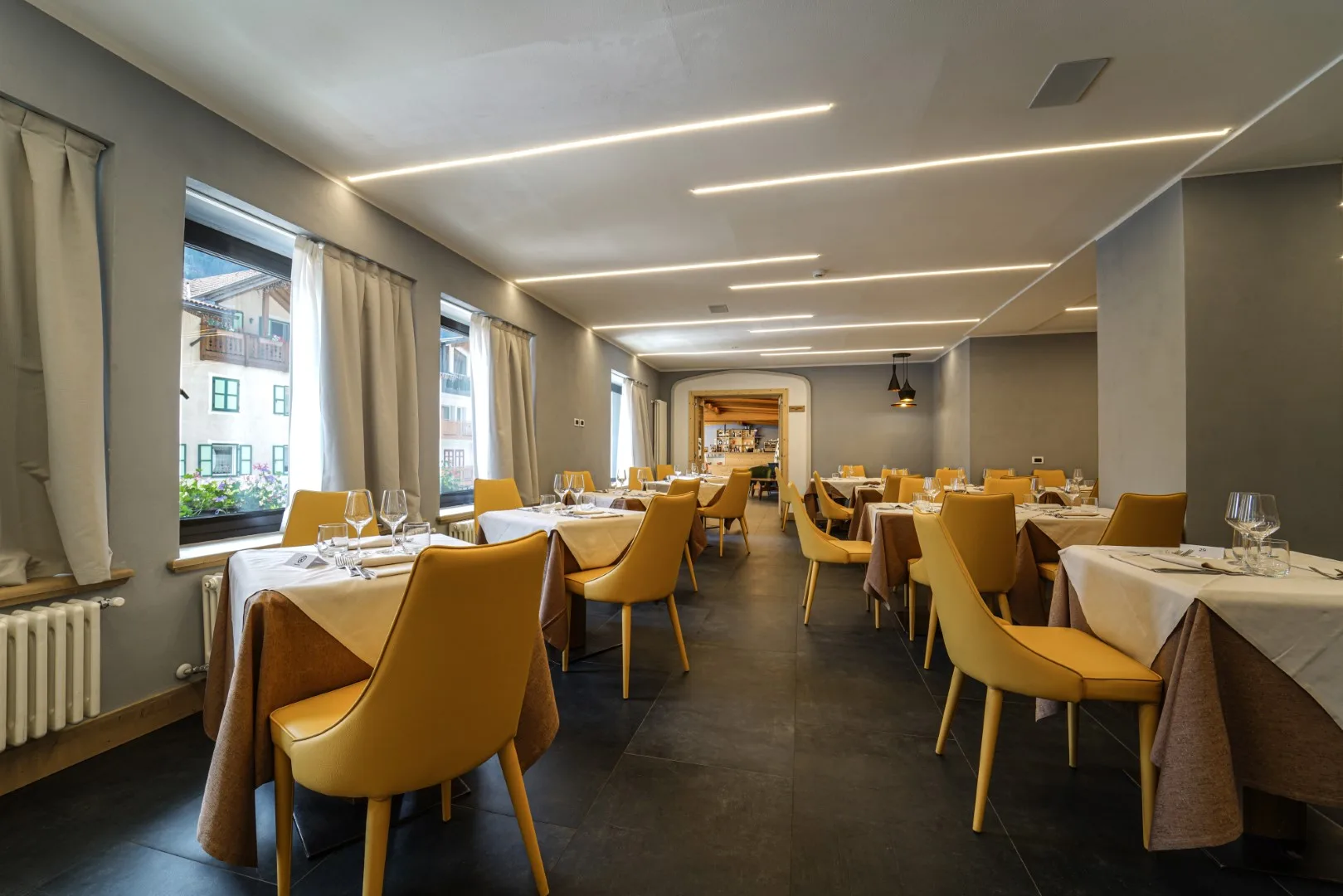 Sala ristorante moderna con sedie gialle, tavoli apparecchiati e illuminazione a led sul soffitto