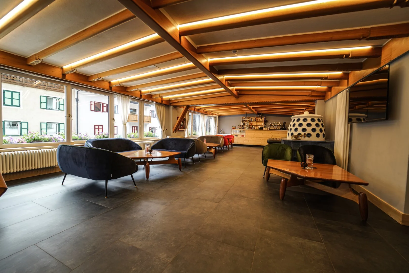Ampia zona lounge con divani, tavolini in legno e grandi finestre affacciate sul paese
