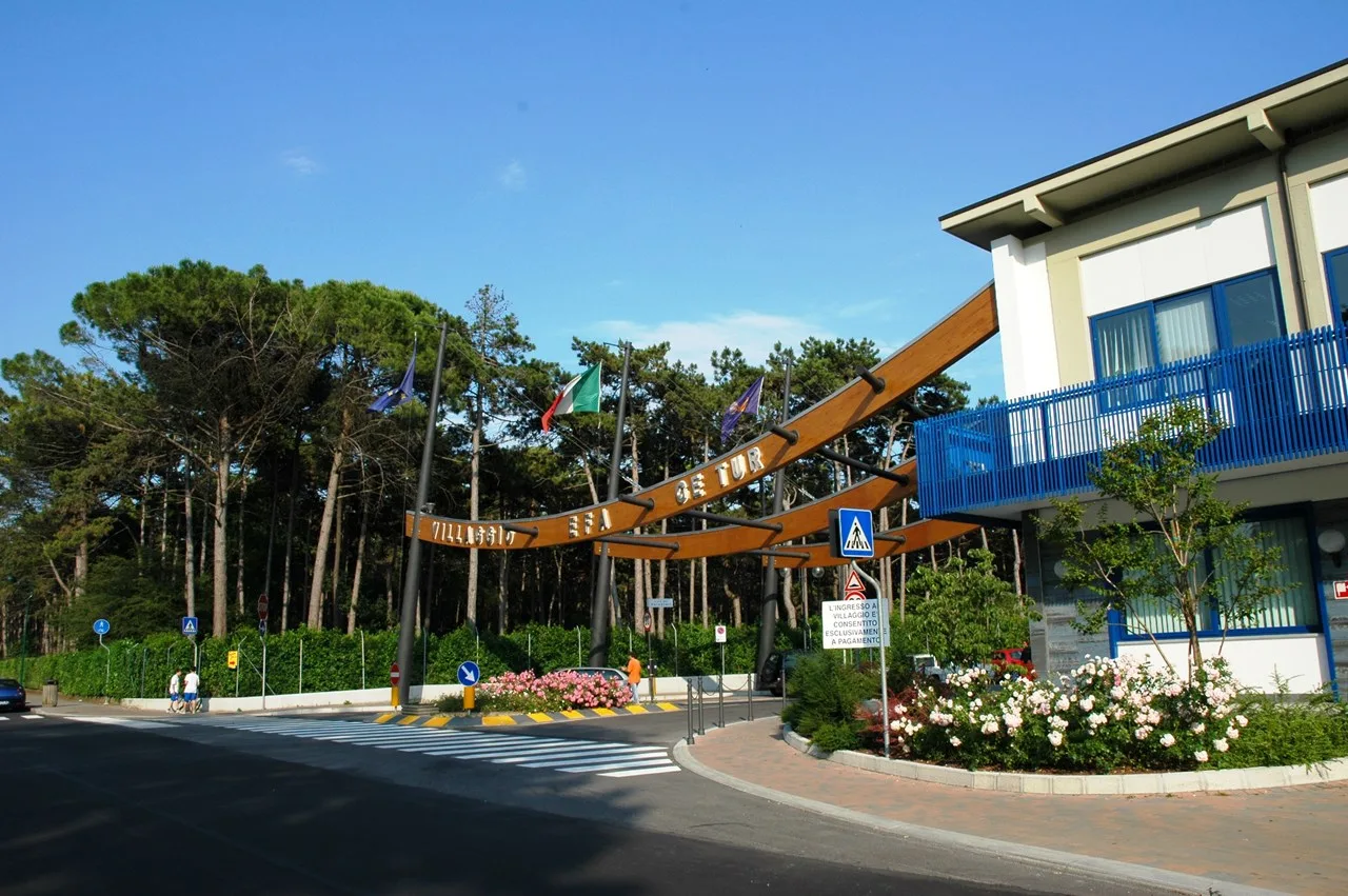 Ingresso del villaggio con arco in legno e bandiere tra i pini
