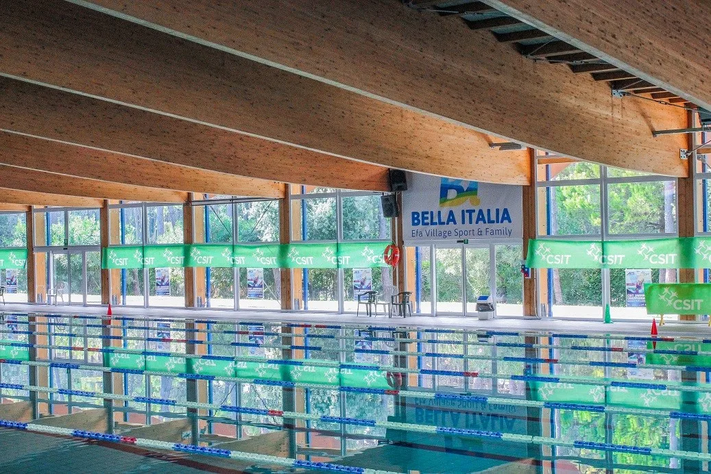 Interno della piscina coperta con corsie e insegna Bella Italia