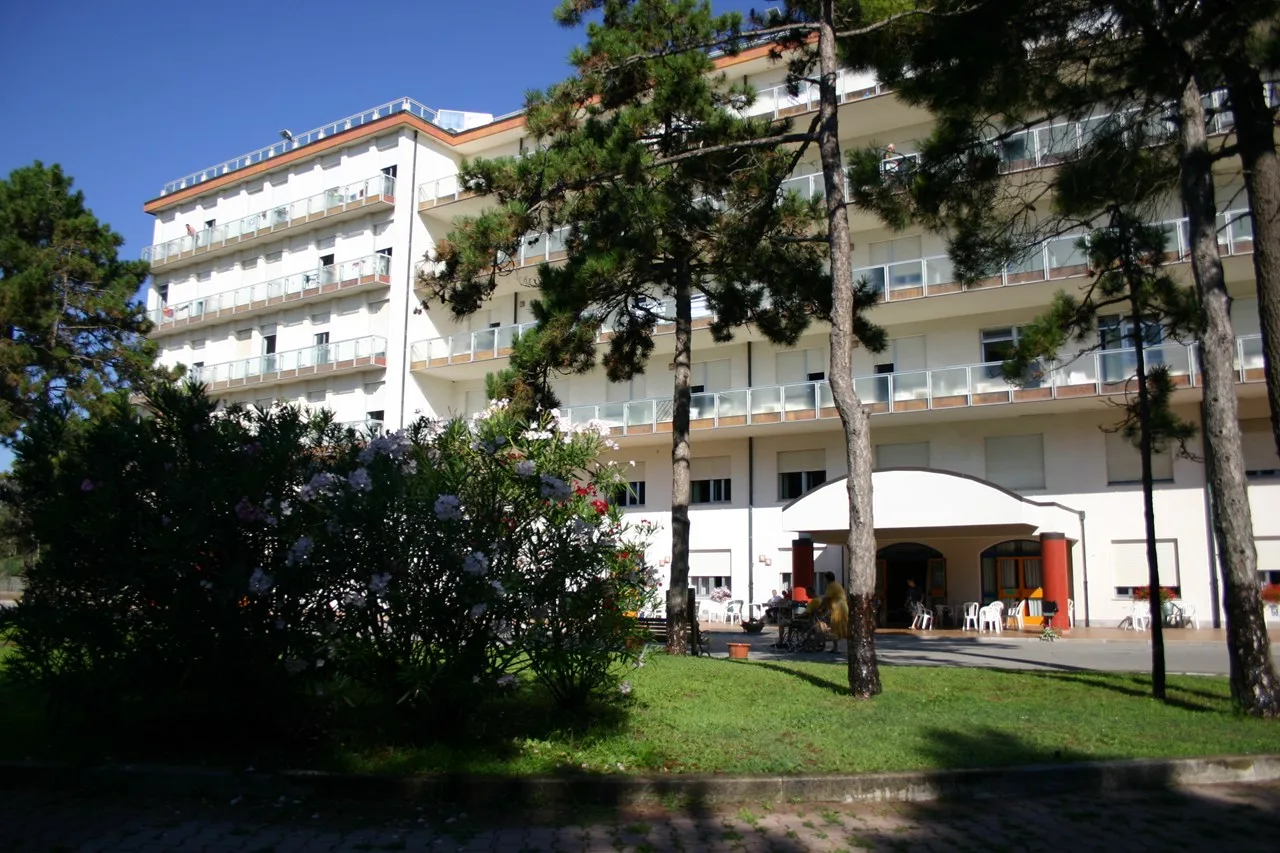 Edificio bianco residenziale con balconi circondato da alberi e fiori