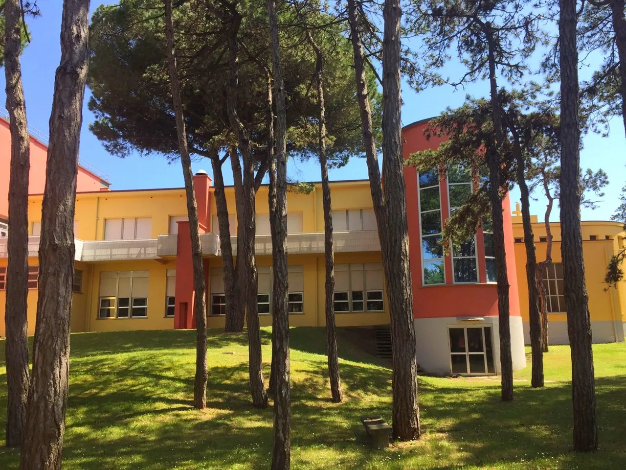 Edificio giallo e arancione visto tra i pini del parco