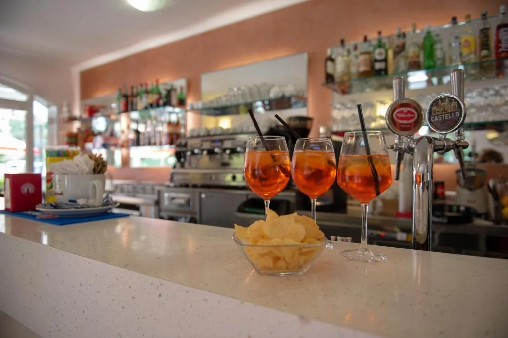 Bancone bar con tre spritz e ciotola di patatine