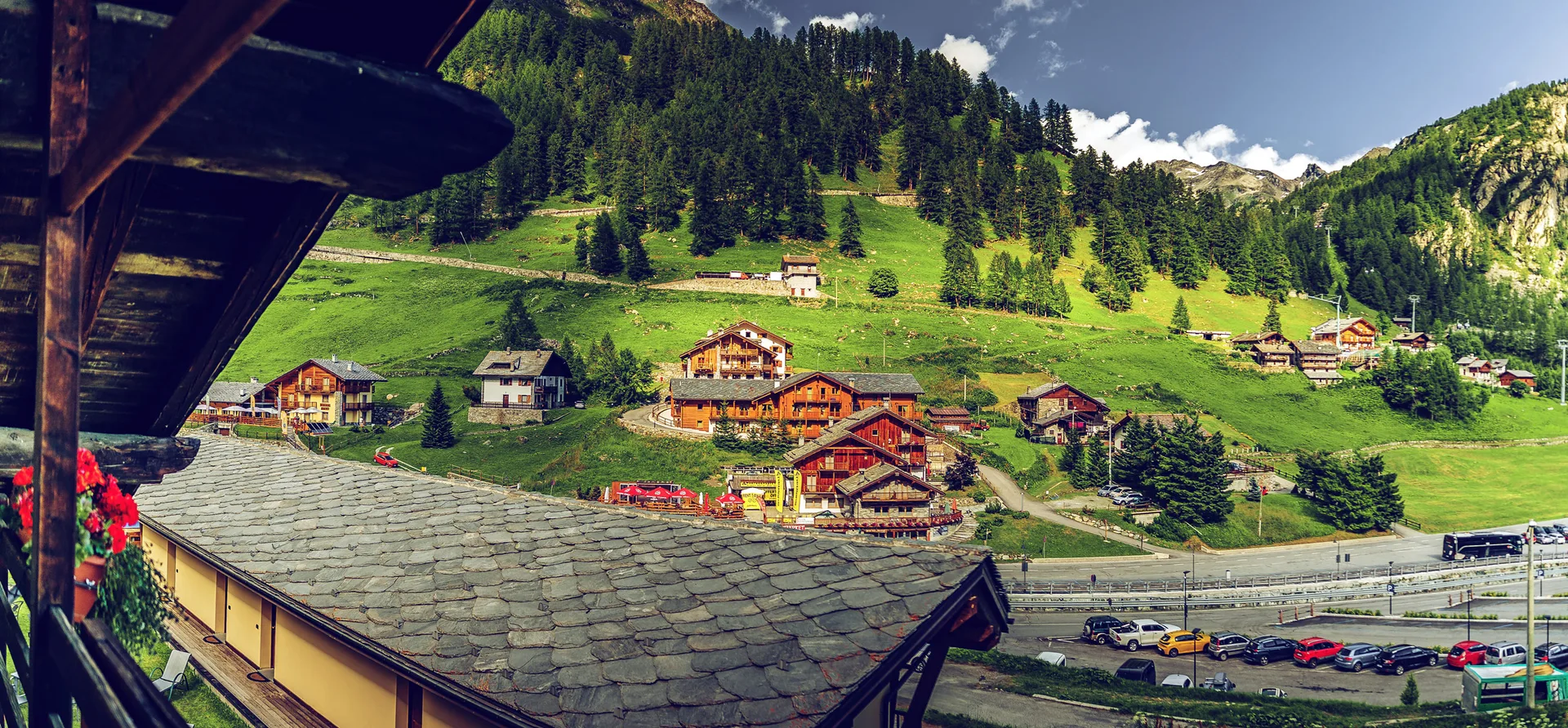 Vista panoramica dal balcone dell'hotel su villaggio alpino, chalet in legno e prati verdi in montagna