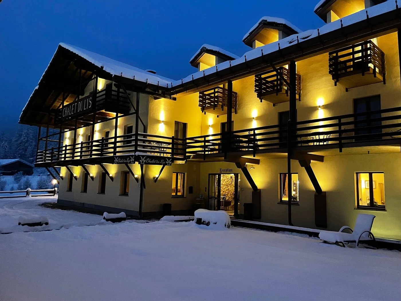 Facciata dello Chalet du Lys illuminata nella neve al crepuscolo con reception e balconi in legno