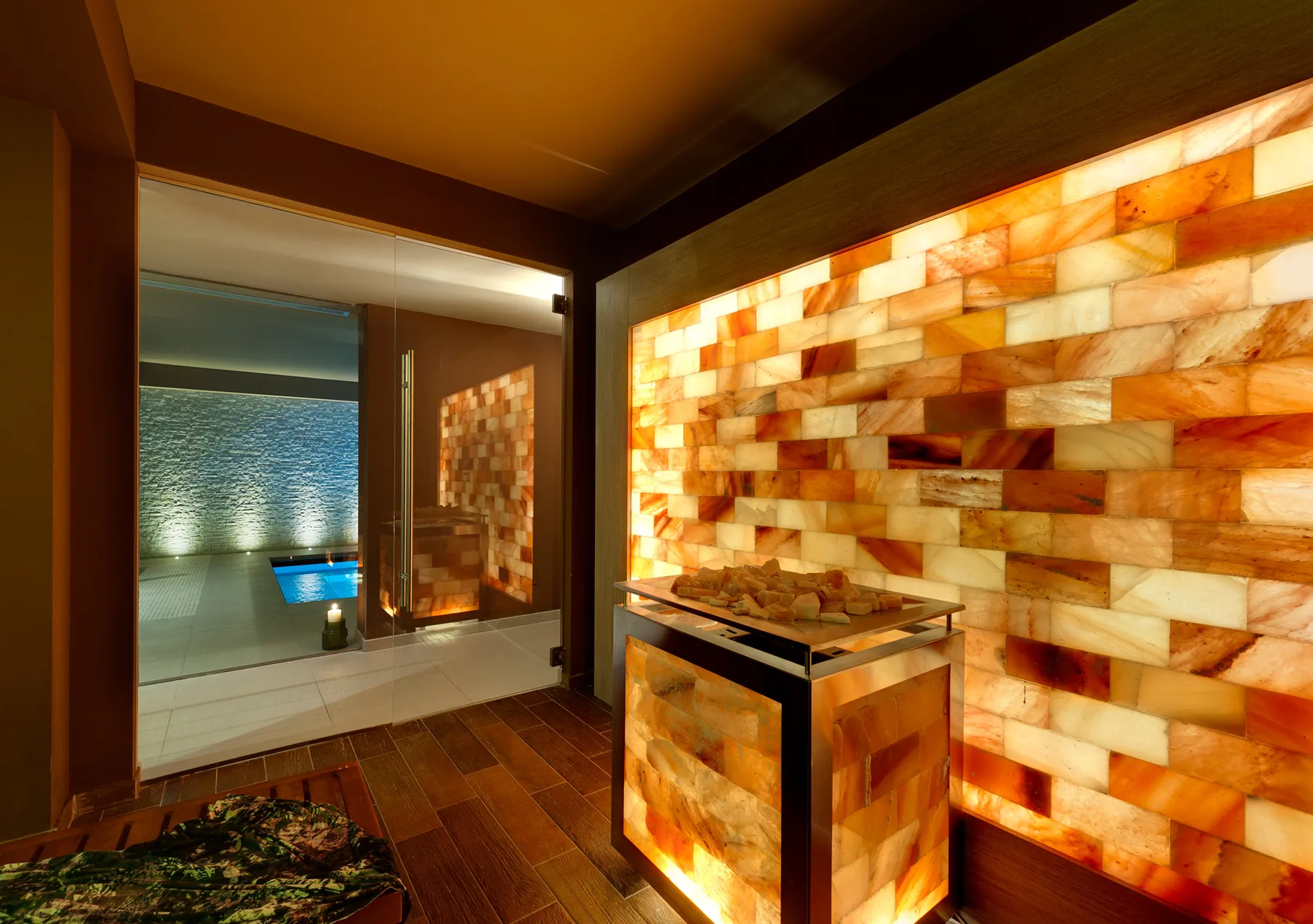 Sauna con parete in sale rosa illuminata e vista sulla piscina interna della spa