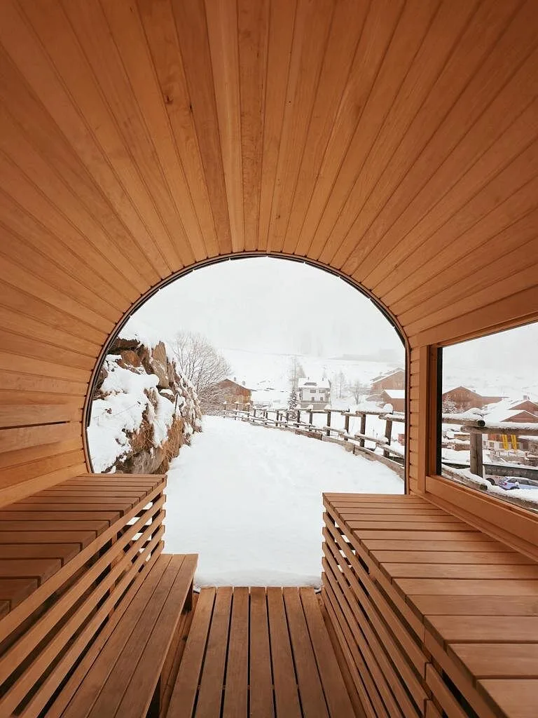 Interno di sauna panoramica in legno con ampia vetrata affacciata sul paesaggio innevato