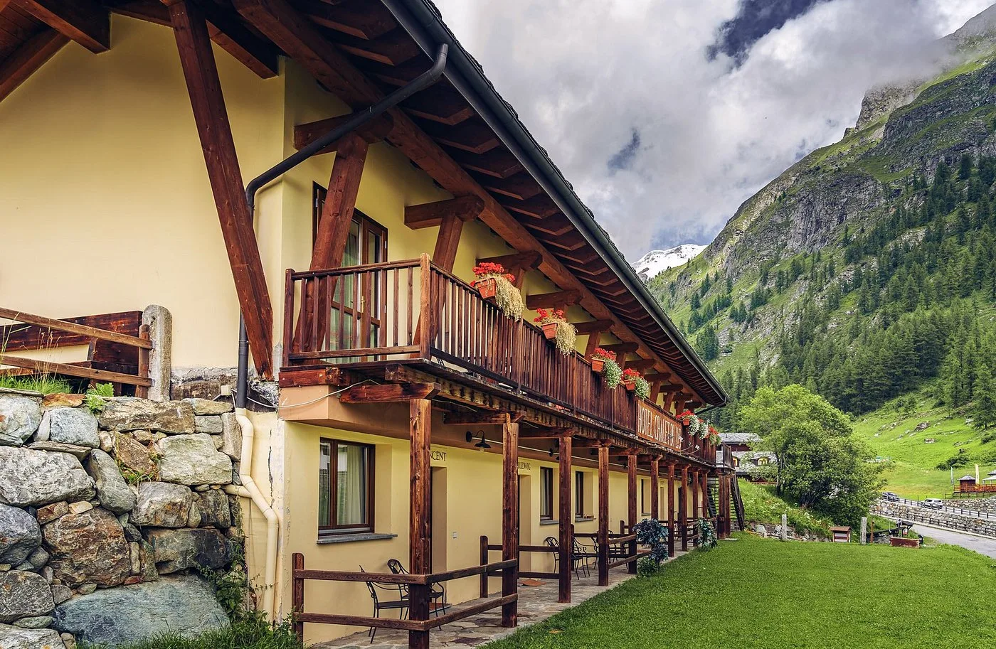 Facciata laterale dell'hotel con balconi in legno fioriti e montagne con vetta innevata
