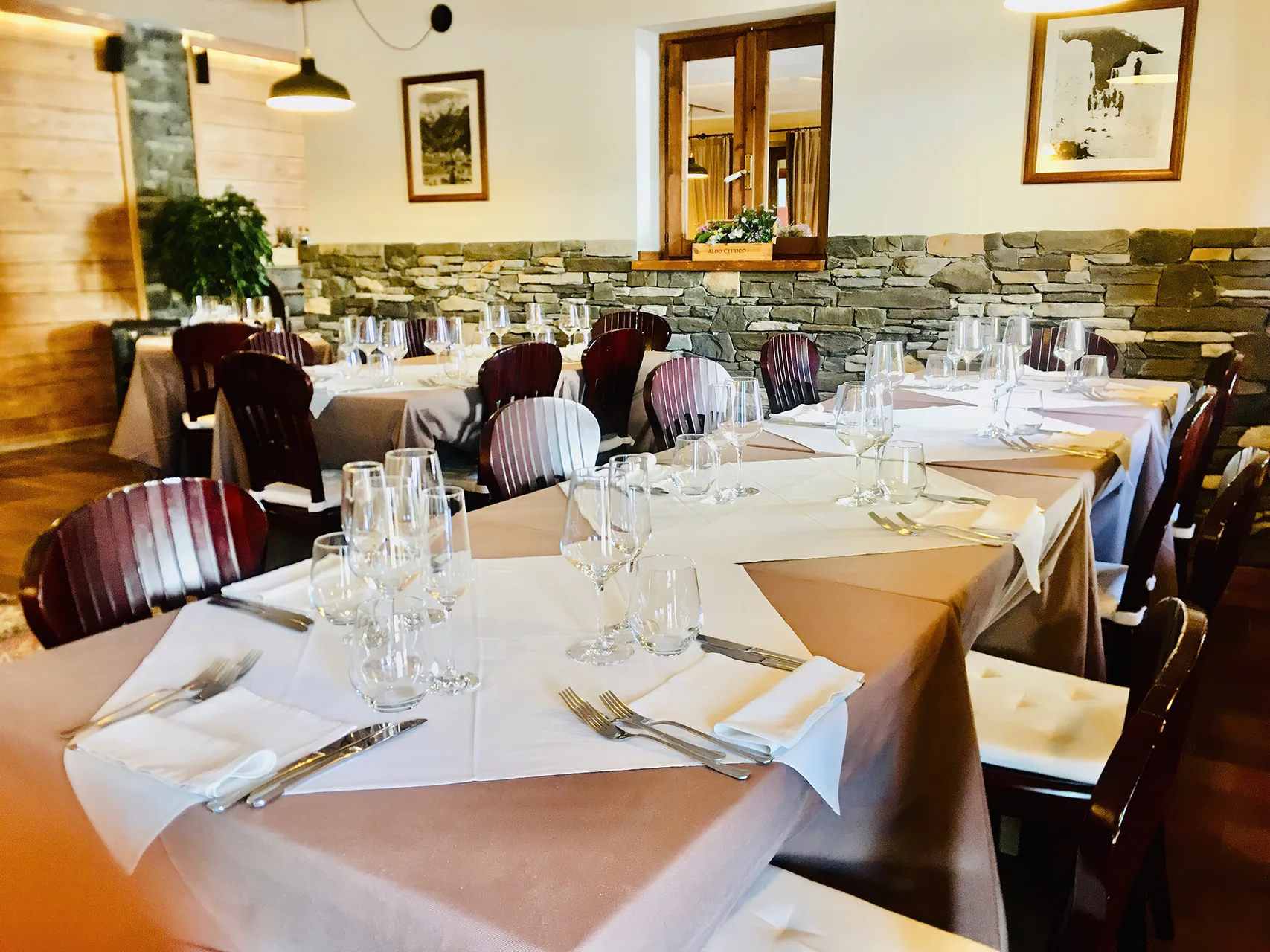 Sala ristorante con tavoli apparecchiati, calici di vino e parete in pietra a vista