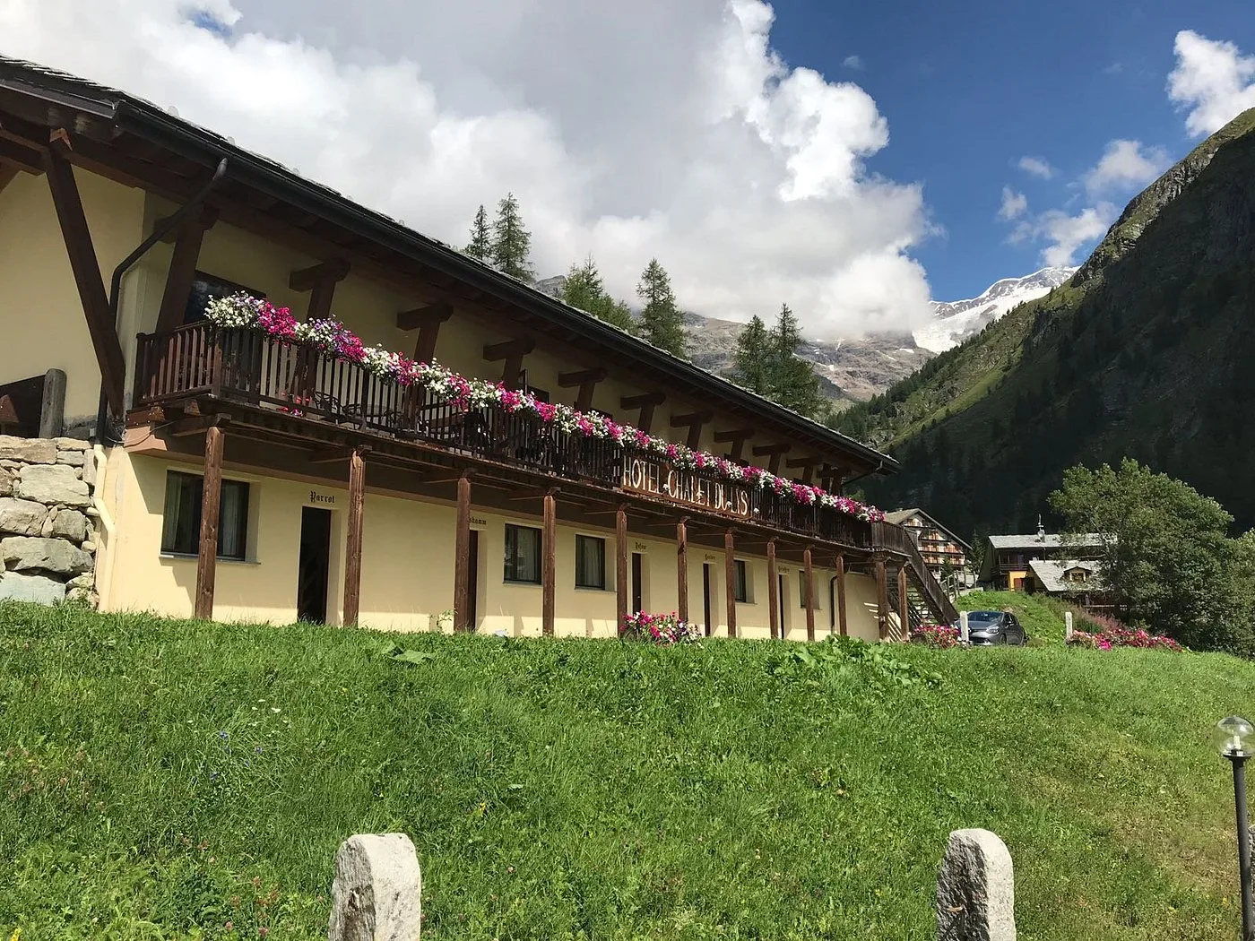 Facciata dell'hotel Chalet du Lys con balcone fiorito e montagne verdi sullo sfondo