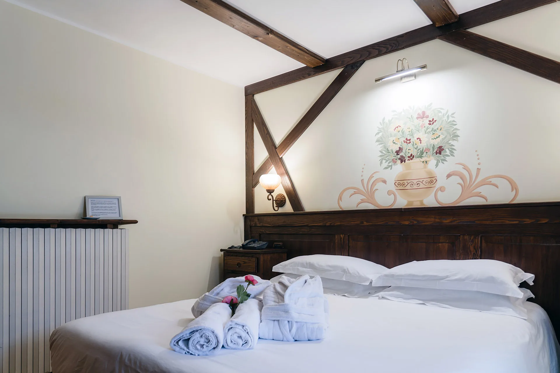Camera matrimoniale con testiera in legno, decorazione floreale dipinta e accappatoi sul letto