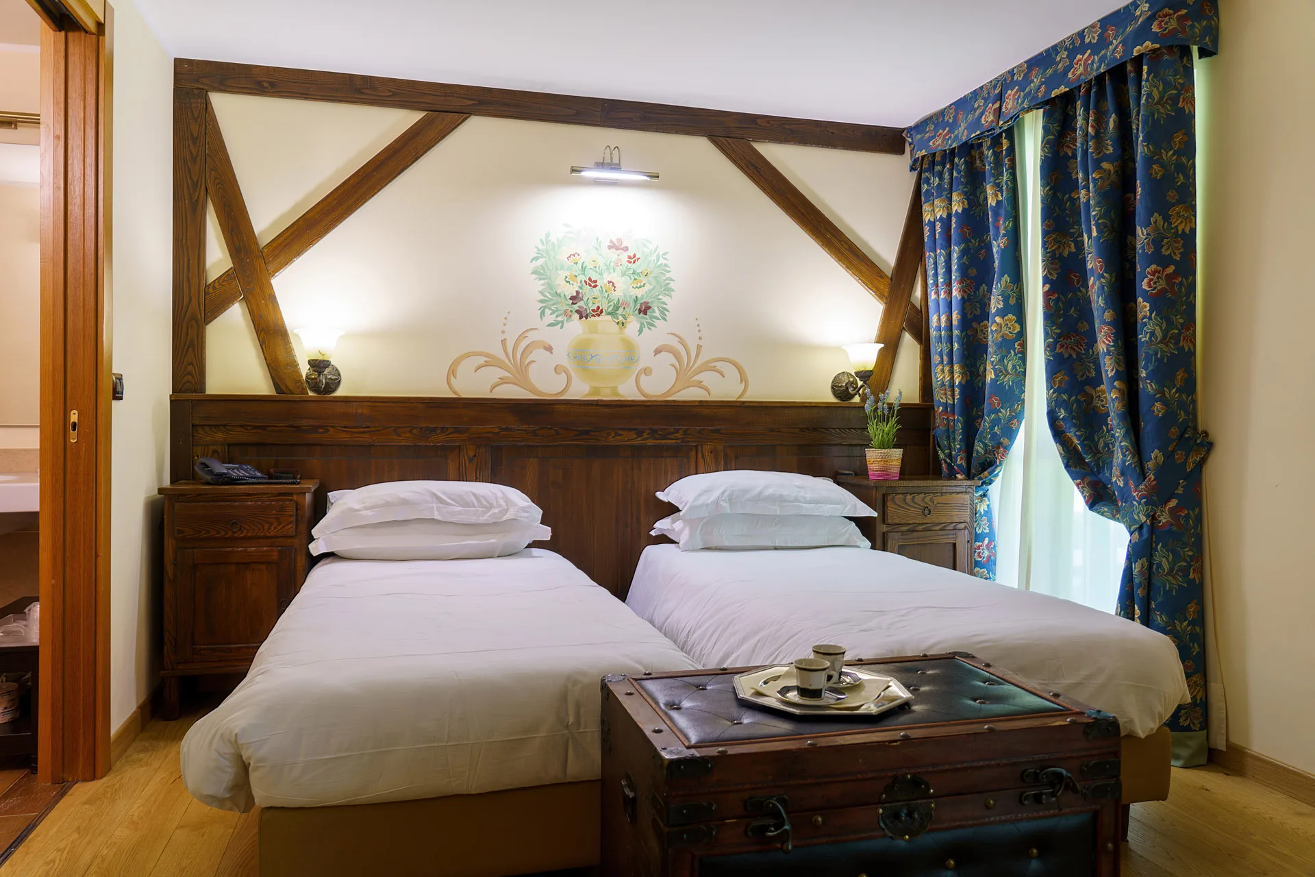 Camera con due letti singoli, testiera in legno decorata e tende blu a fiori