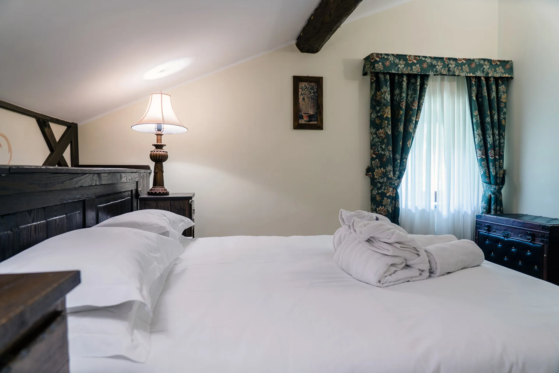 Camera con letto matrimoniale, tende floreali verdi, lampada e baule d'epoca