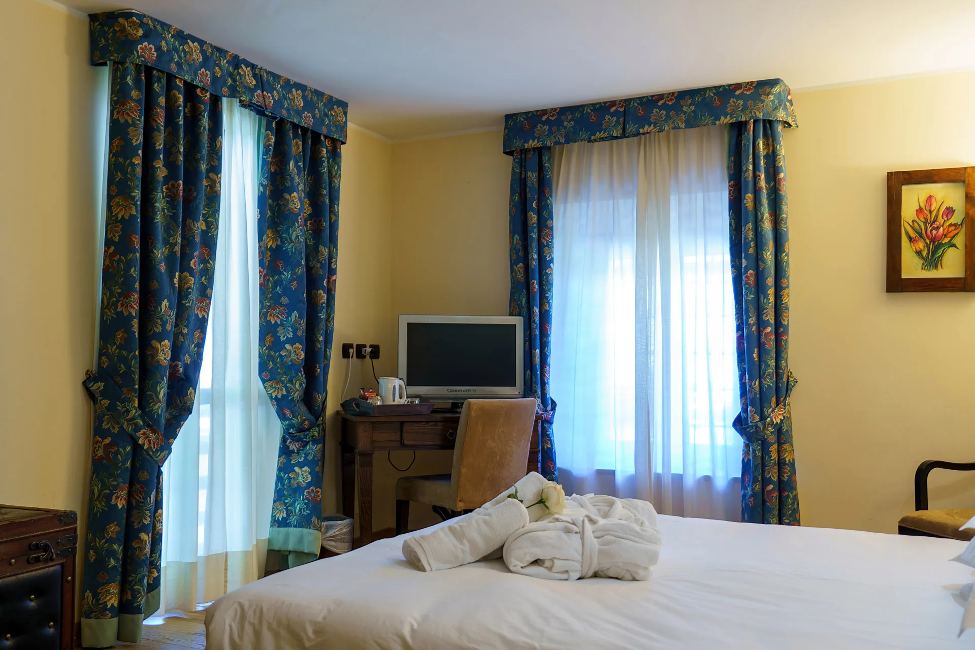 Camera con tende blu floreali, scrivania con TV e accappatoi sul letto
