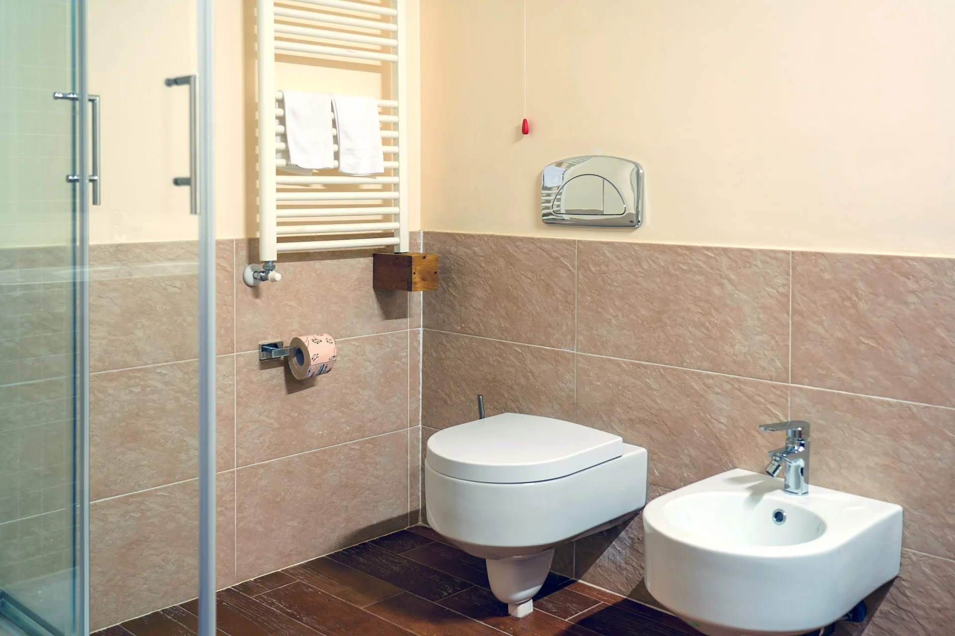 Bagno con doccia in vetro, wc e bidet sospesi e piastrelle in pietra beige