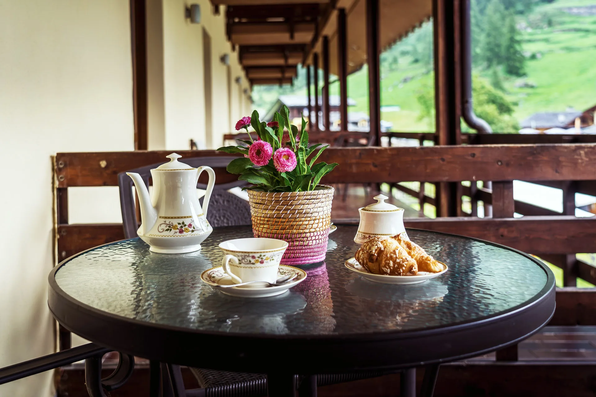 Colazione servita sul balcone con teiera in porcellana, cornetto e fiori con vista sulla vallata