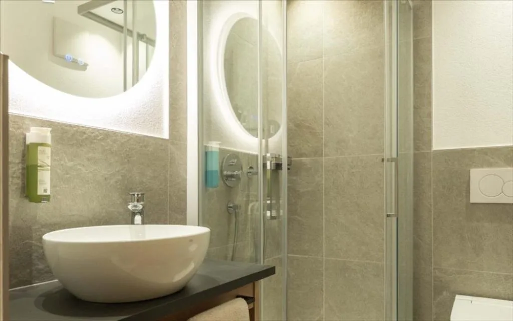 Bagno moderno con lavabo tondo, specchio illuminato e doccia in vetro