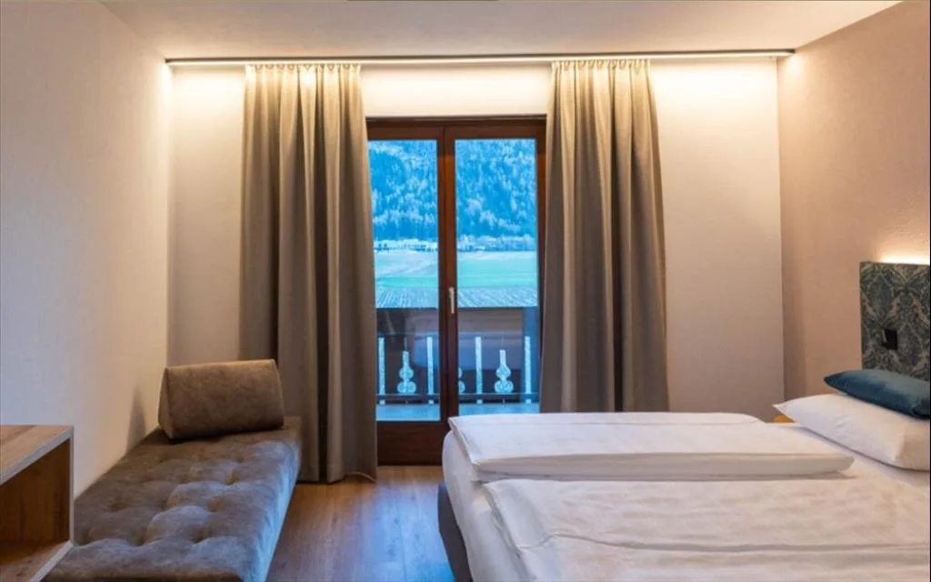 Camera con letto matrimoniale, panca imbottita e vista sui prati alpini