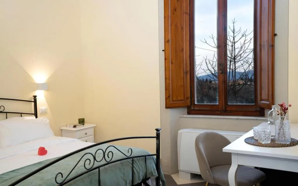 Camera con letto in ferro battuto, scrivania e finestra con vista sul borgo