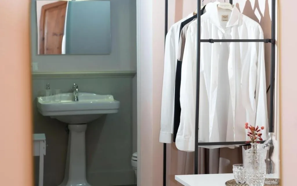 Appendiabiti con camicie bianche e specchio che riflette il lavabo del bagno