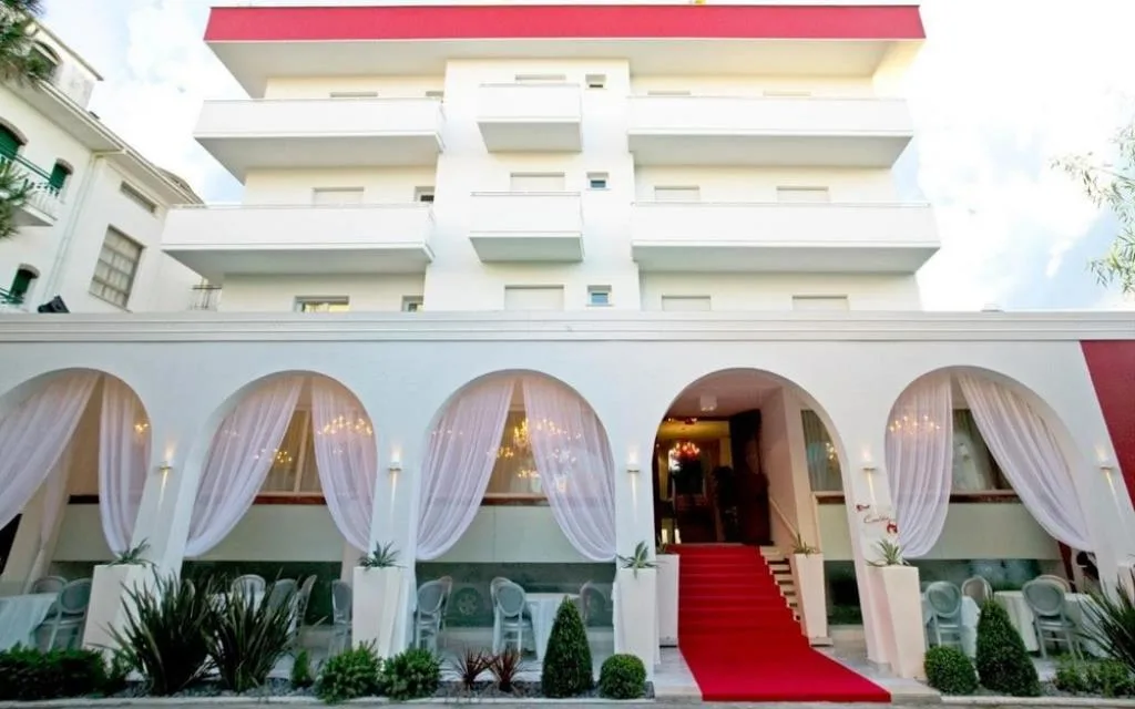 Facciata dell'hotel con archi drappeggiati di tende bianche e tappeto rosso all'ingresso