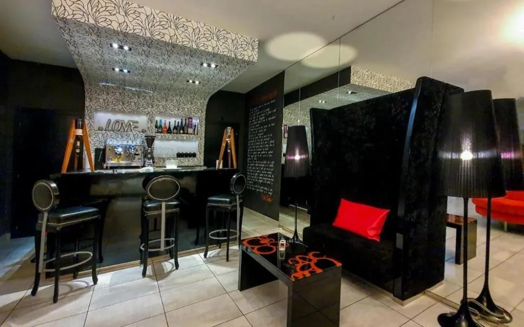 Area bar interna con bancone nero, sgabelli, divano elegante e cuscino rosso